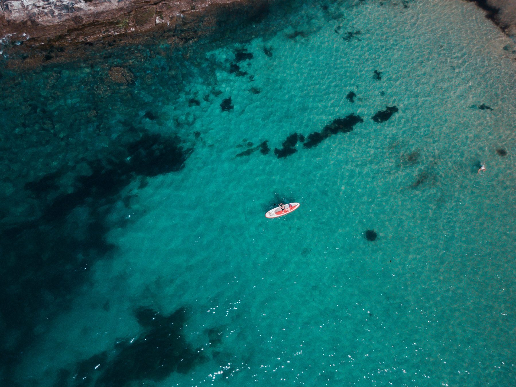 A paddleboard floating above turquoise sea and submerged rocks